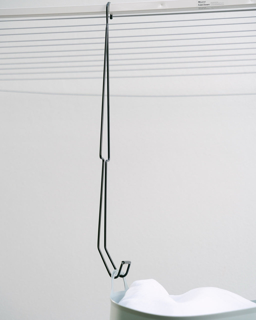 A full-length Hang Easy Basket Hanger hooked on the clothesline frame and holding a basket handle